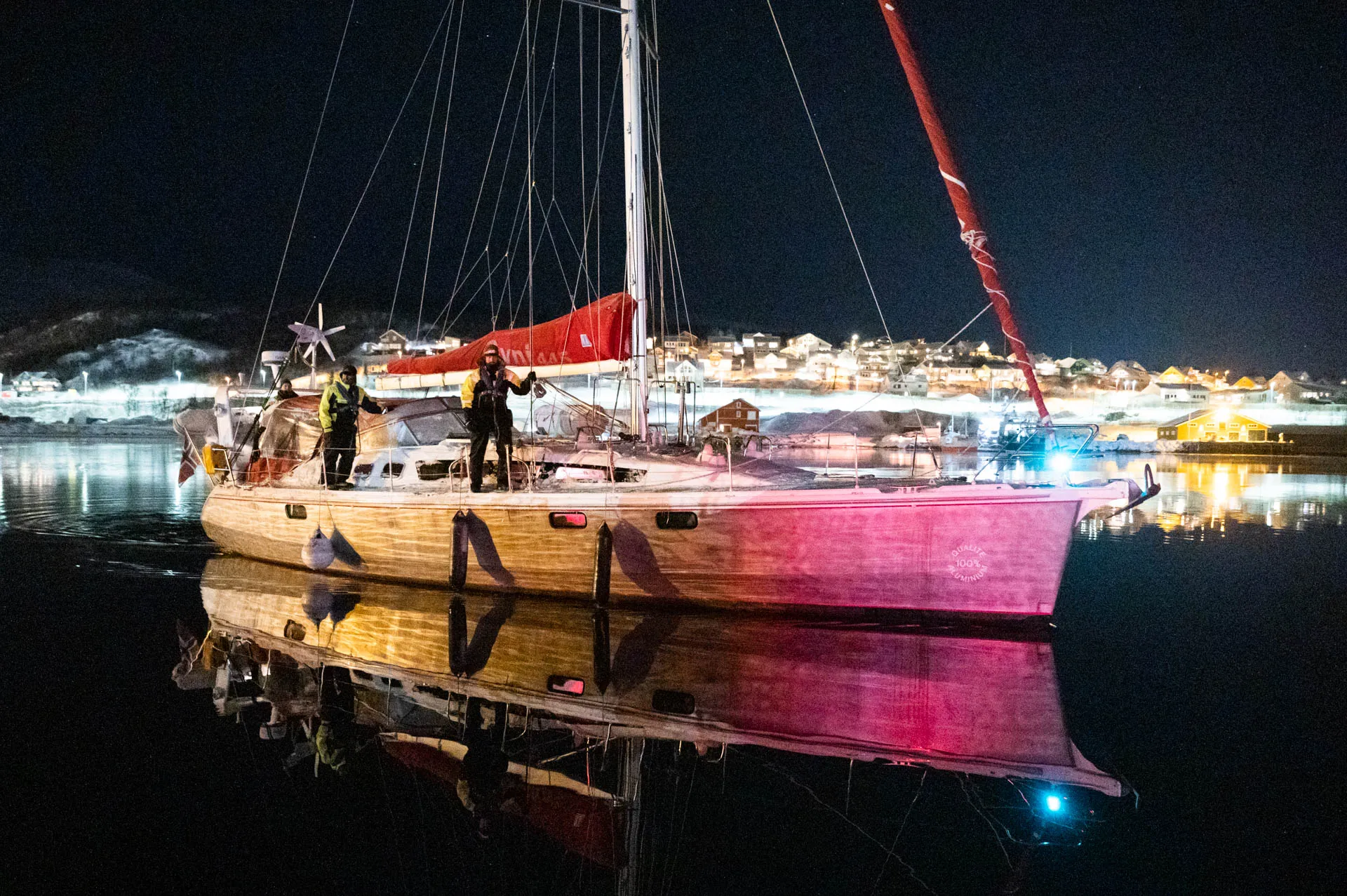 Segelschiff mit Crew läuft nachts in einen beleuchteten Hafen im Norden ein